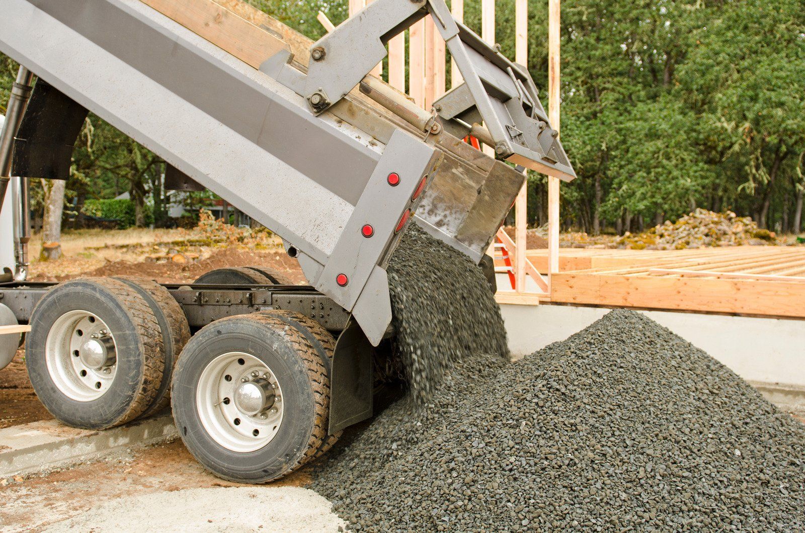 A dump truck pouring a load of gravel onto the ground at a construction site.
