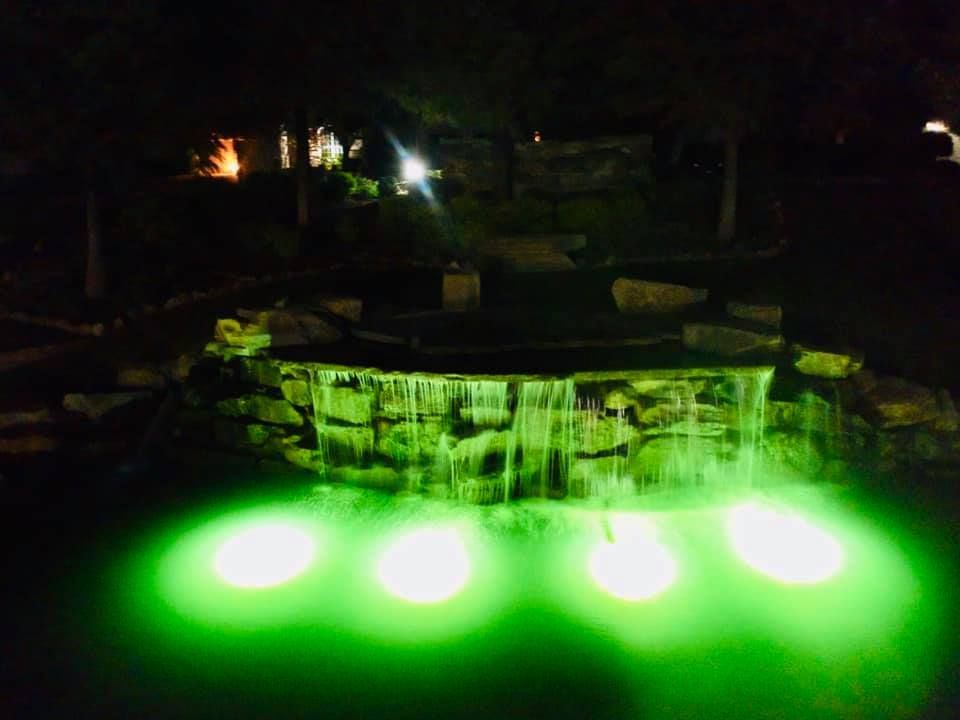 A waterfall is lit up with green lights at night.