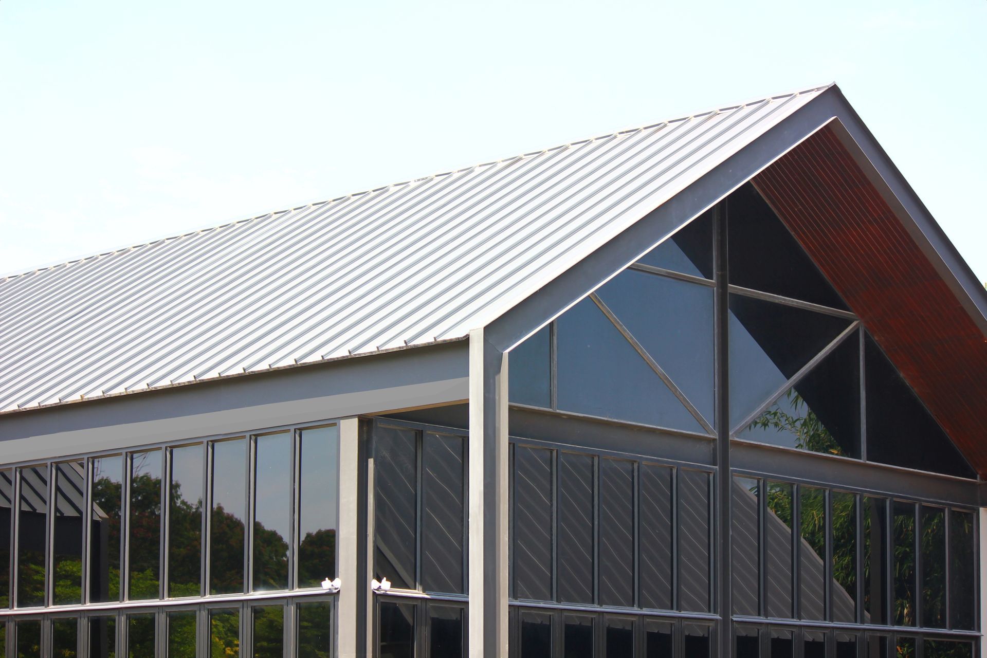 Modern building with ACM Panel roof, glass windows, and gray metal frame under a clear sky.