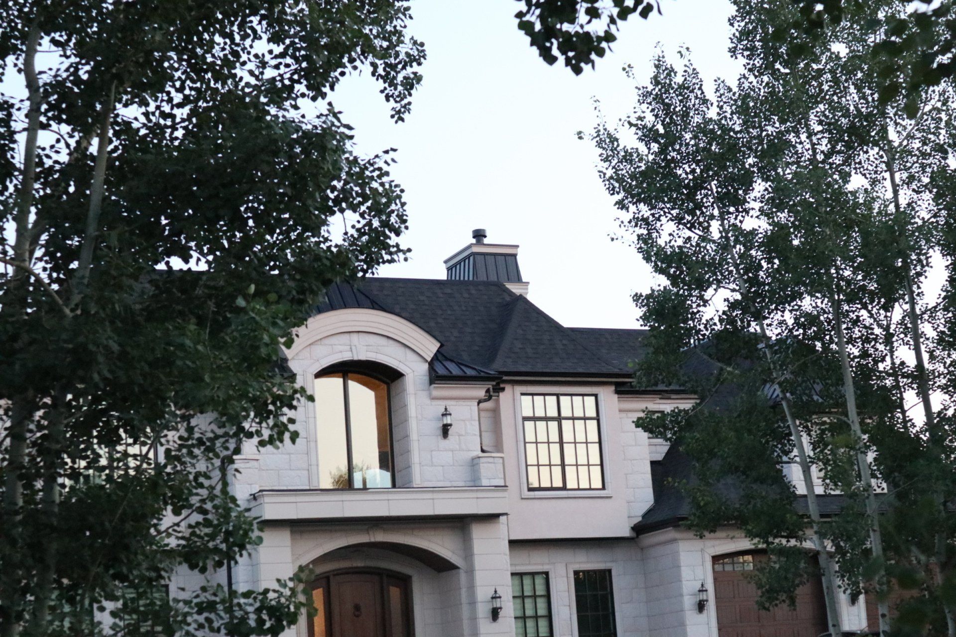 A large white house with a black metal roof is surrounded by trees