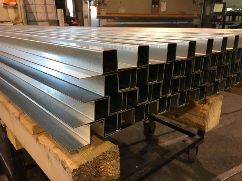 Stacks of shiny, metal, channel-shaped beams on a wooden pallet in a factory setting.