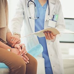 Doctor holding patient's hand, reviewing file. Light blue scrubs, white coat.