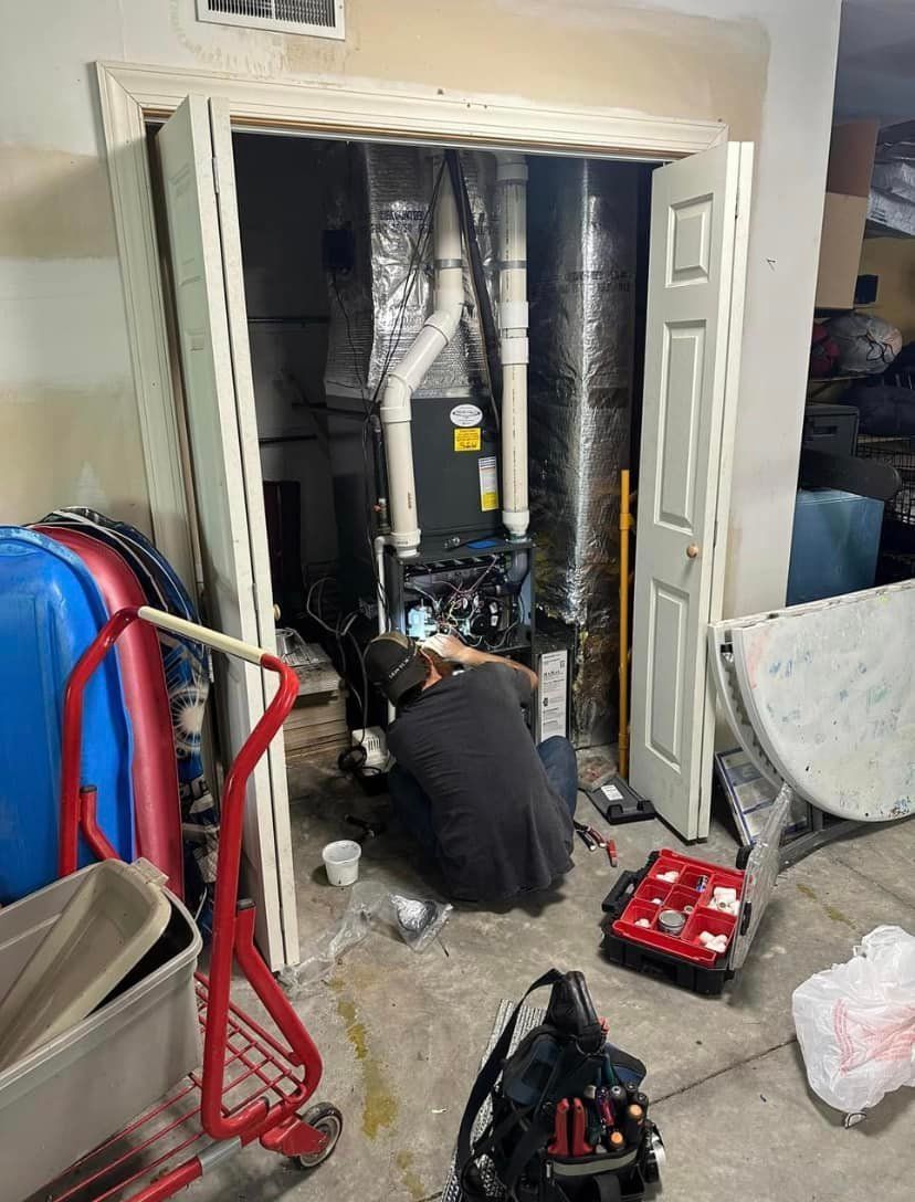 A person working on HVAC equipment inside a utility closet, with tools scattered around.