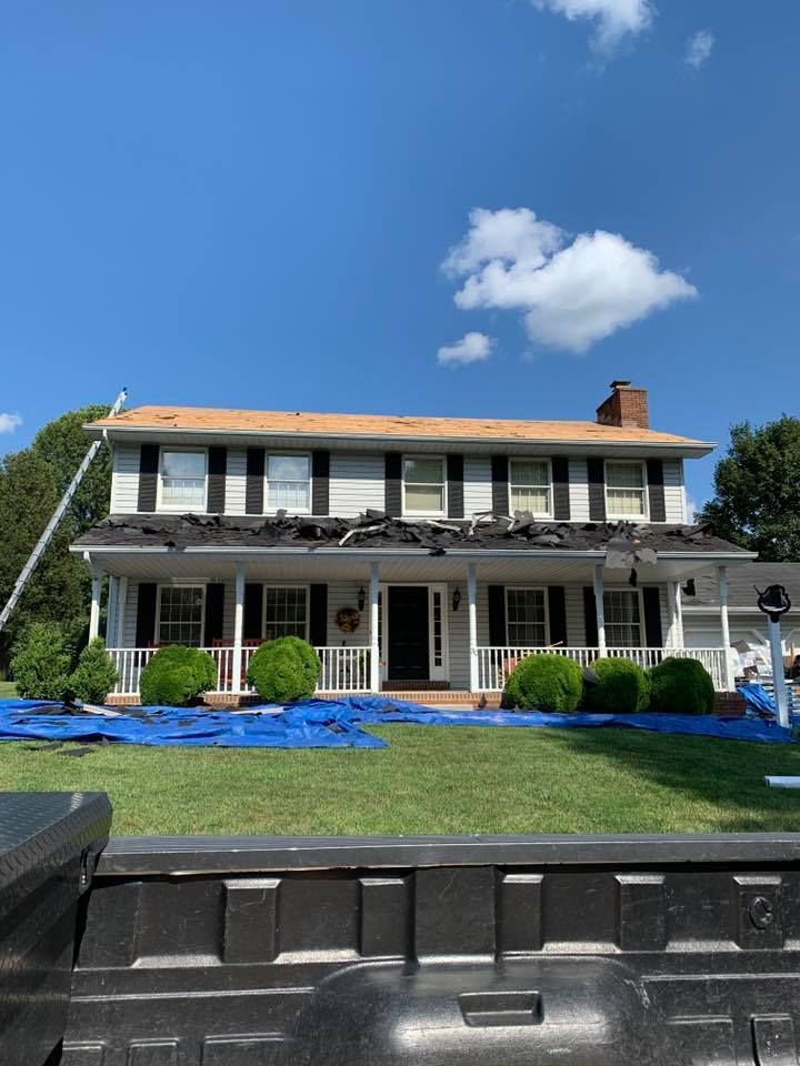 House with roof in progress of being replaced, blue tarps on lawn.