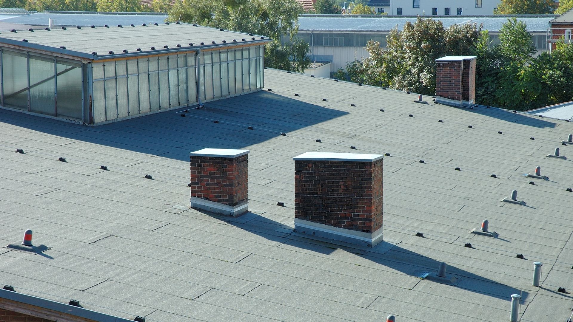 View of a gray rooftop with brick chimneys and a glass-paneled structure.