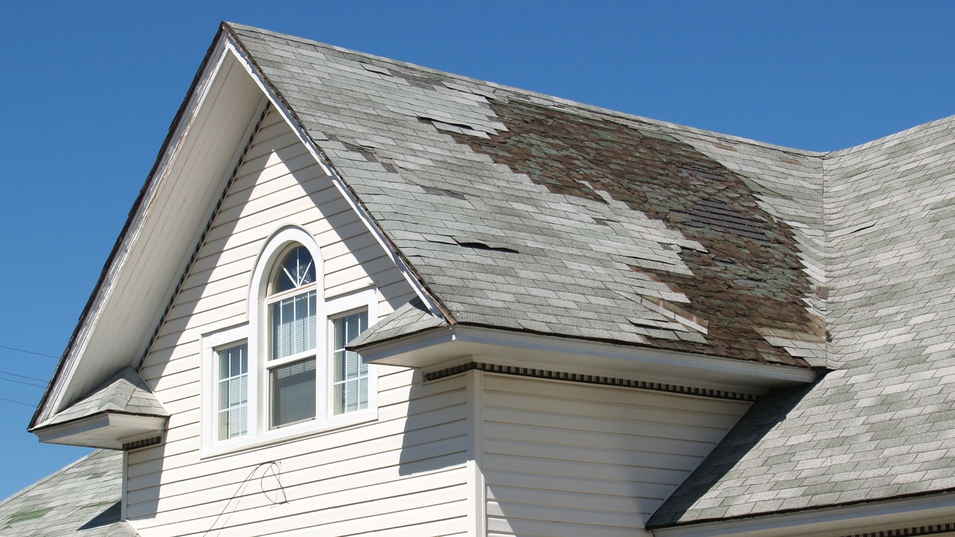 White house with damaged, weathered roof under a clear blue sky.