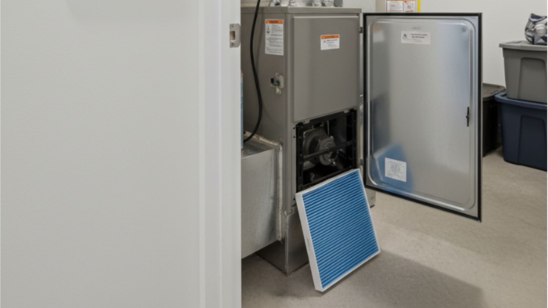 Furnace with open door, blue air filter removed. Grey appliance in a room.