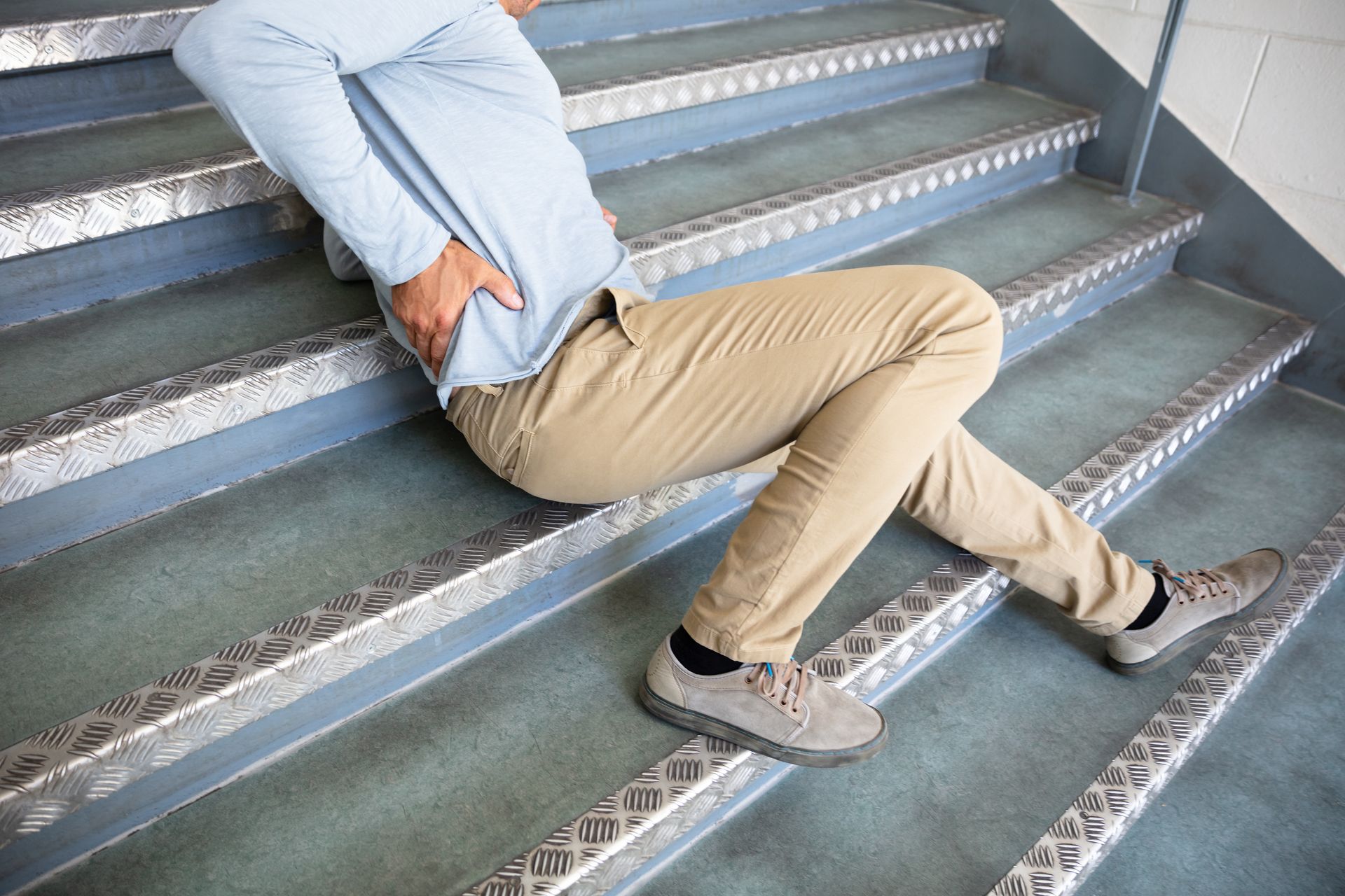 Person sprawled on metal stairs, clutching back in pain.