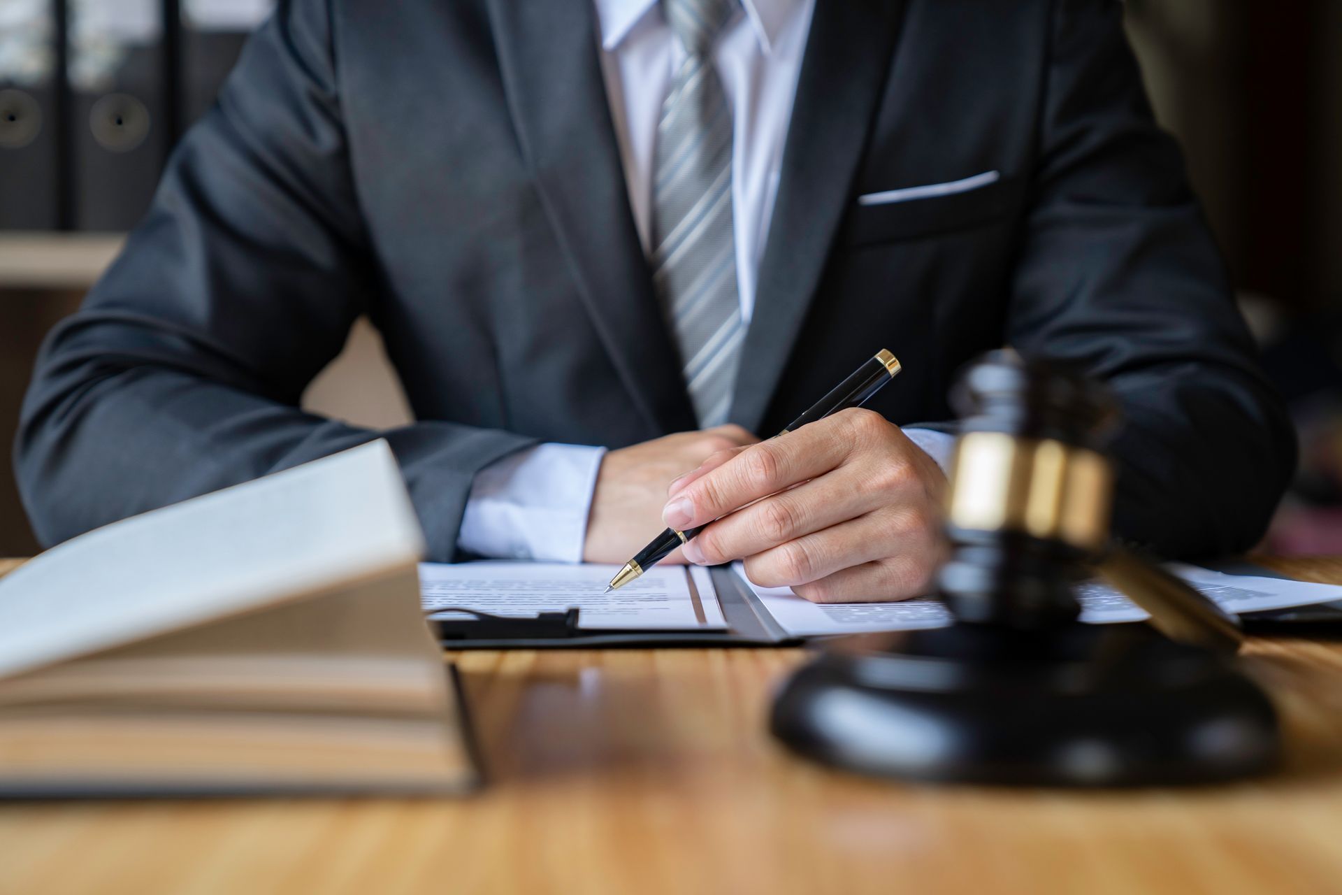 Person in suit writing at a desk, gavel in the foreground, legal documents.