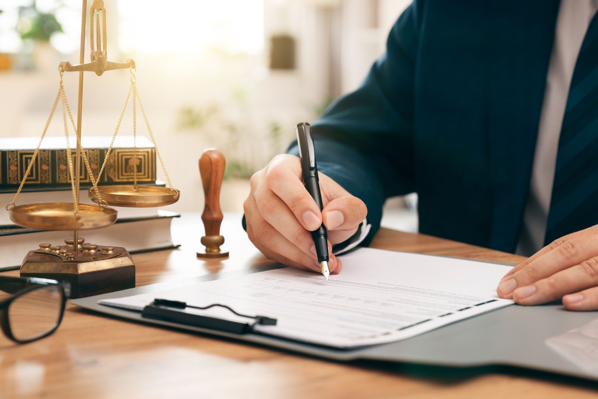 Lawyer signing documents at desk with scales of justice and books.