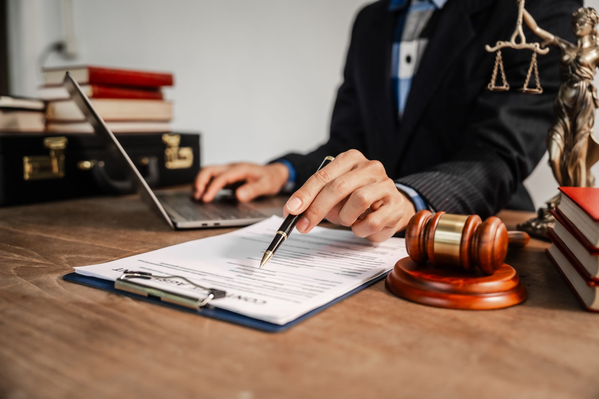 Lawyer in suit pointing at paperwork with laptop, gavel, books, and statue of justice.