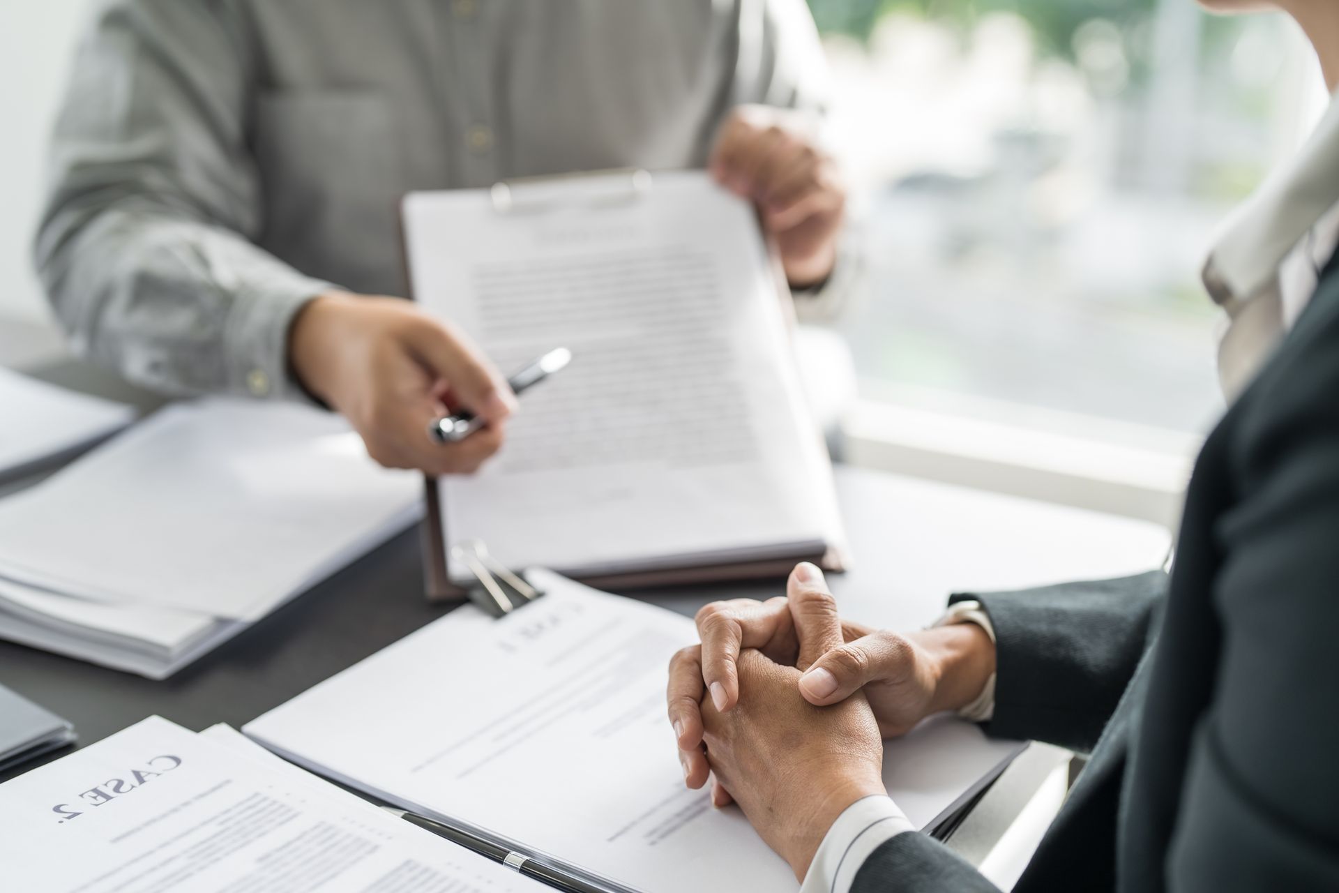 Person showing documents to another person at a desk.