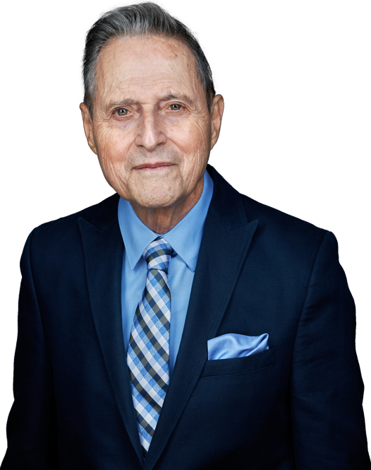 Man in a navy suit and blue shirt, with a patterned tie and pocket square, looking at the camera.