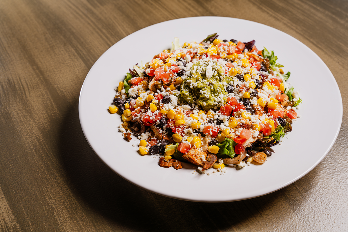 Salad with guacamole, corn, black beans, tomatoes, and cheese on a white plate.