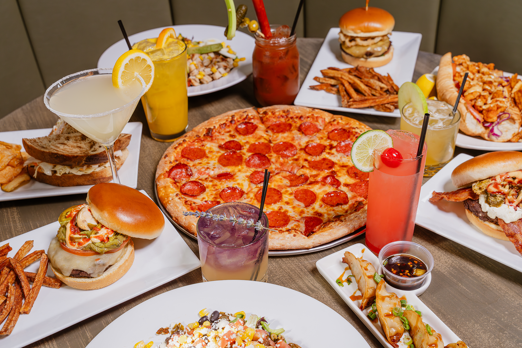 Table of food: pizza, burgers, sandwiches, fries, and cocktails.