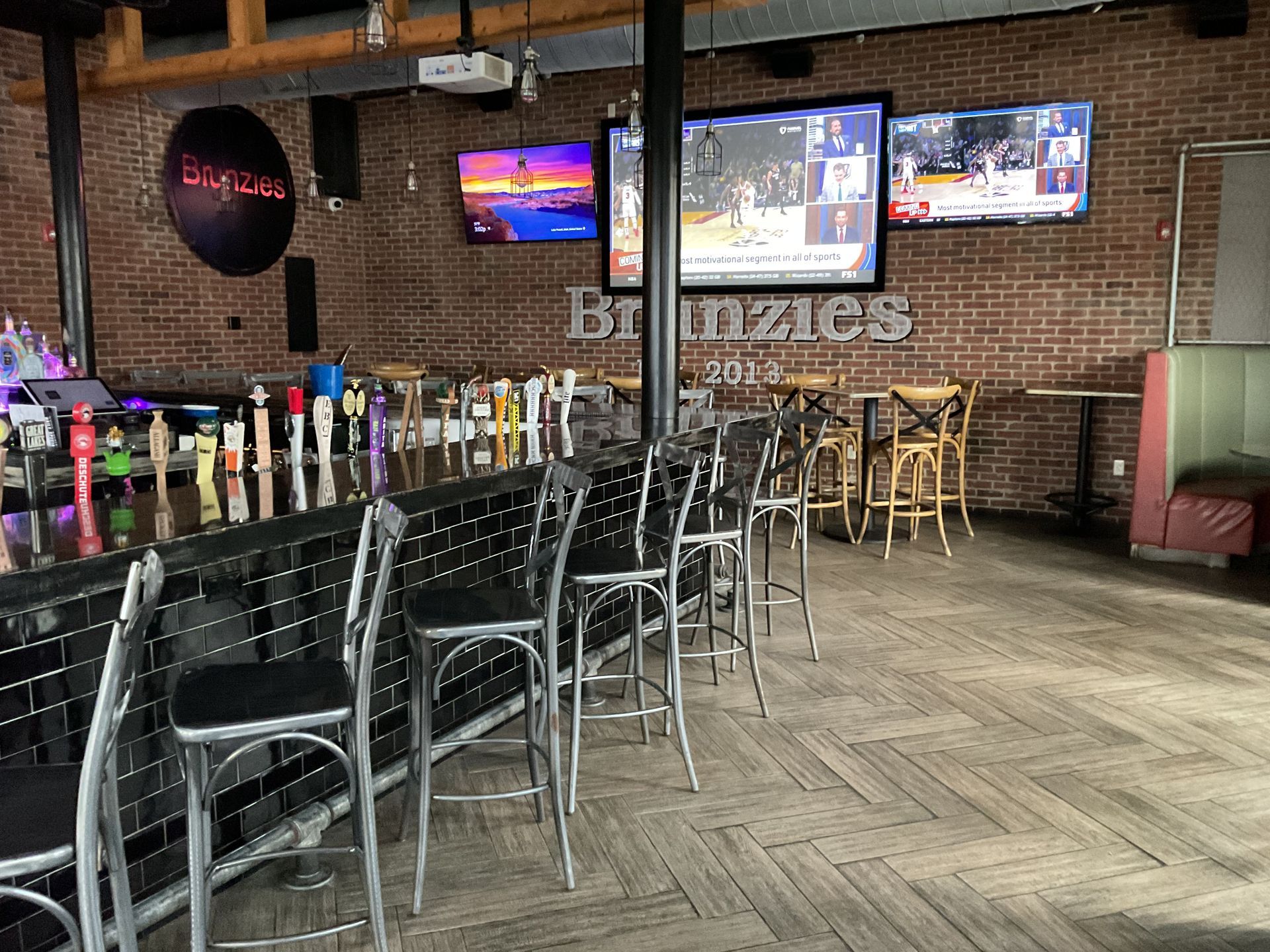 Interior of a bar, brick wall, multiple TVs showing sports, barstools, and beer taps.