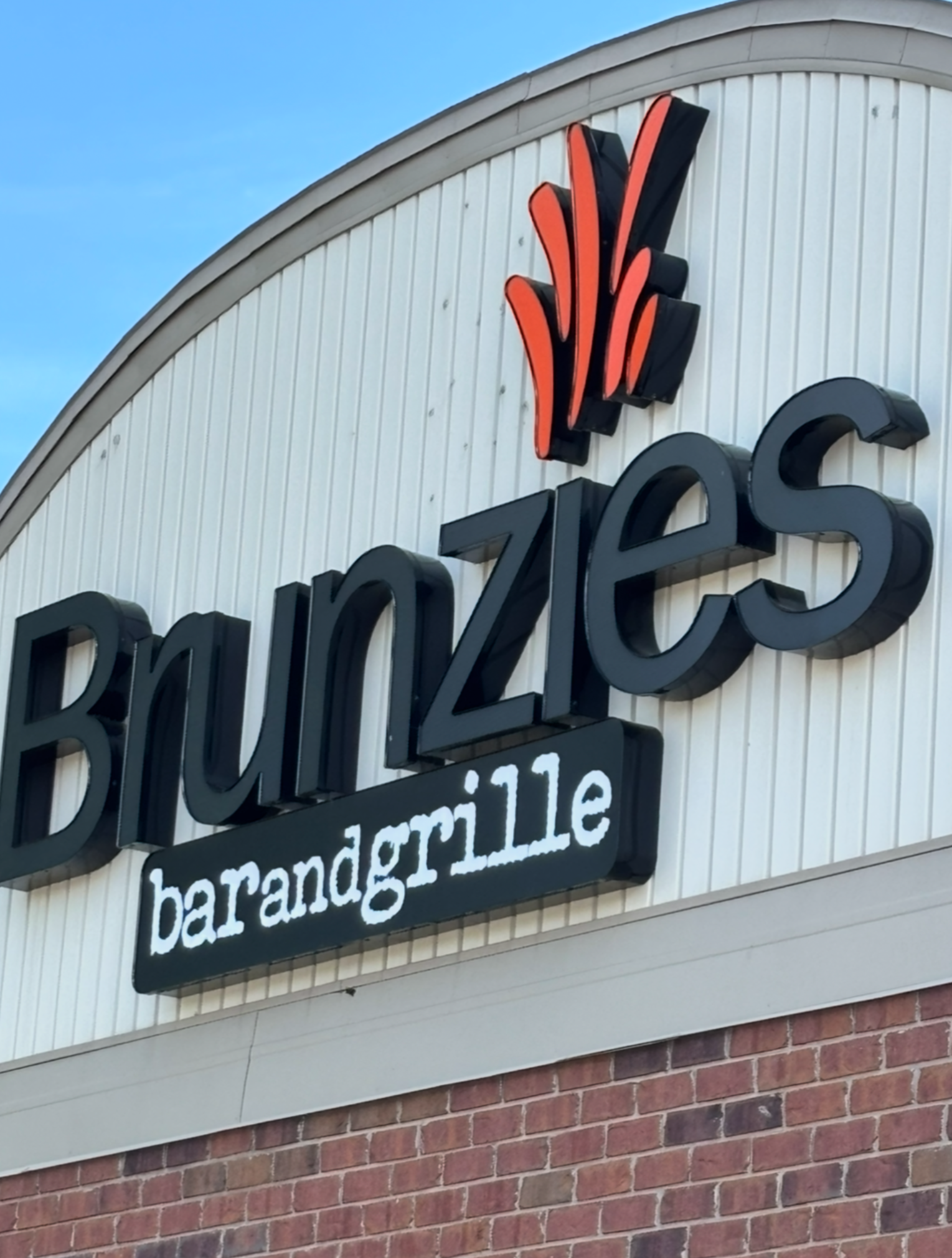 Brunzies bar and grille sign; black letters on a white building. Orange/red stylized flame above the name.