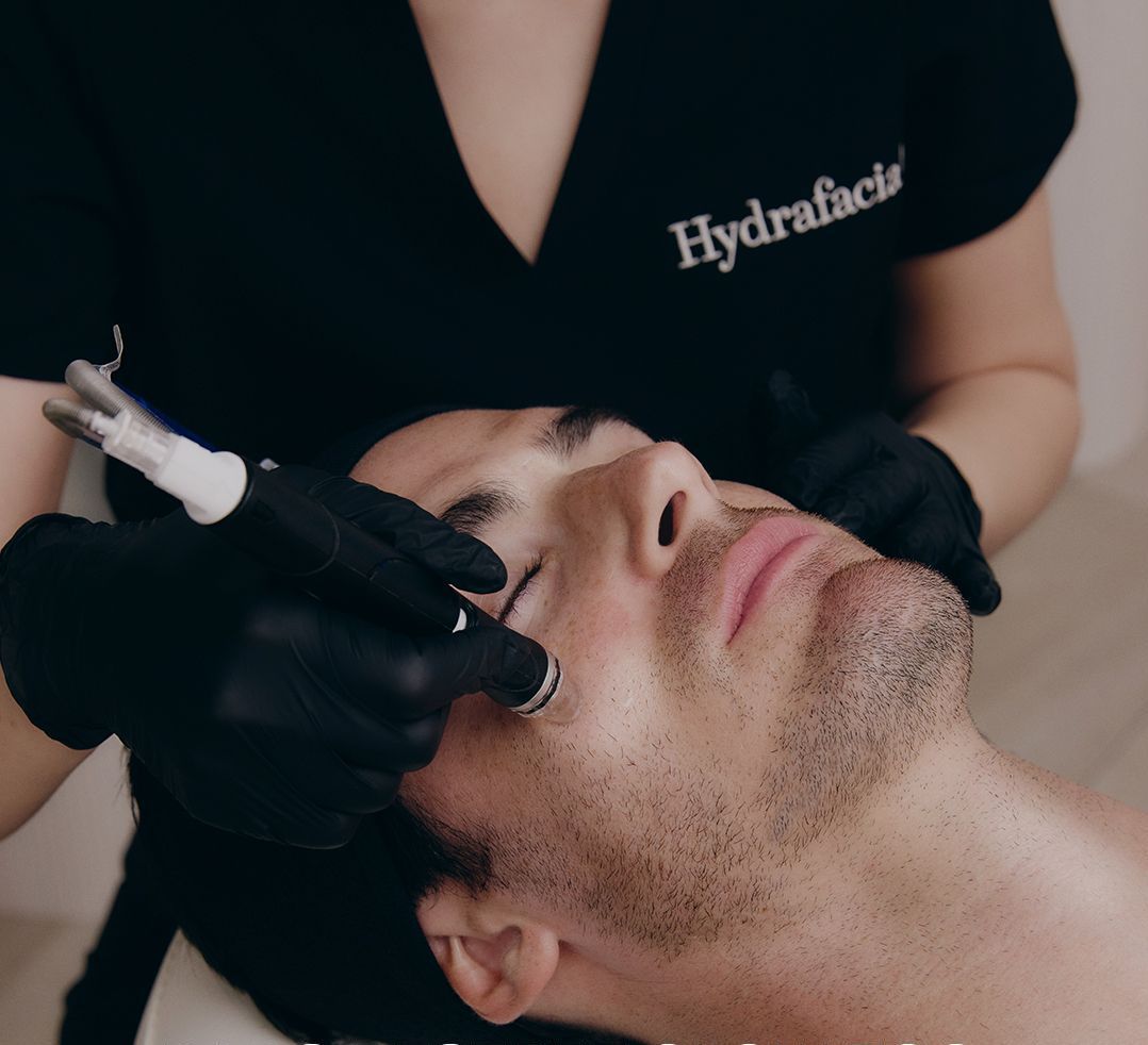 Man receiving a Hydrafacial treatment; esthetician using a device on his face.