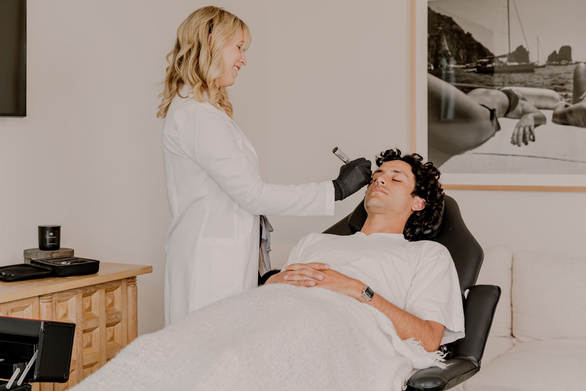 Woman with closed eyes smiles, touching her cheek, against a light pink background, appearing happy.