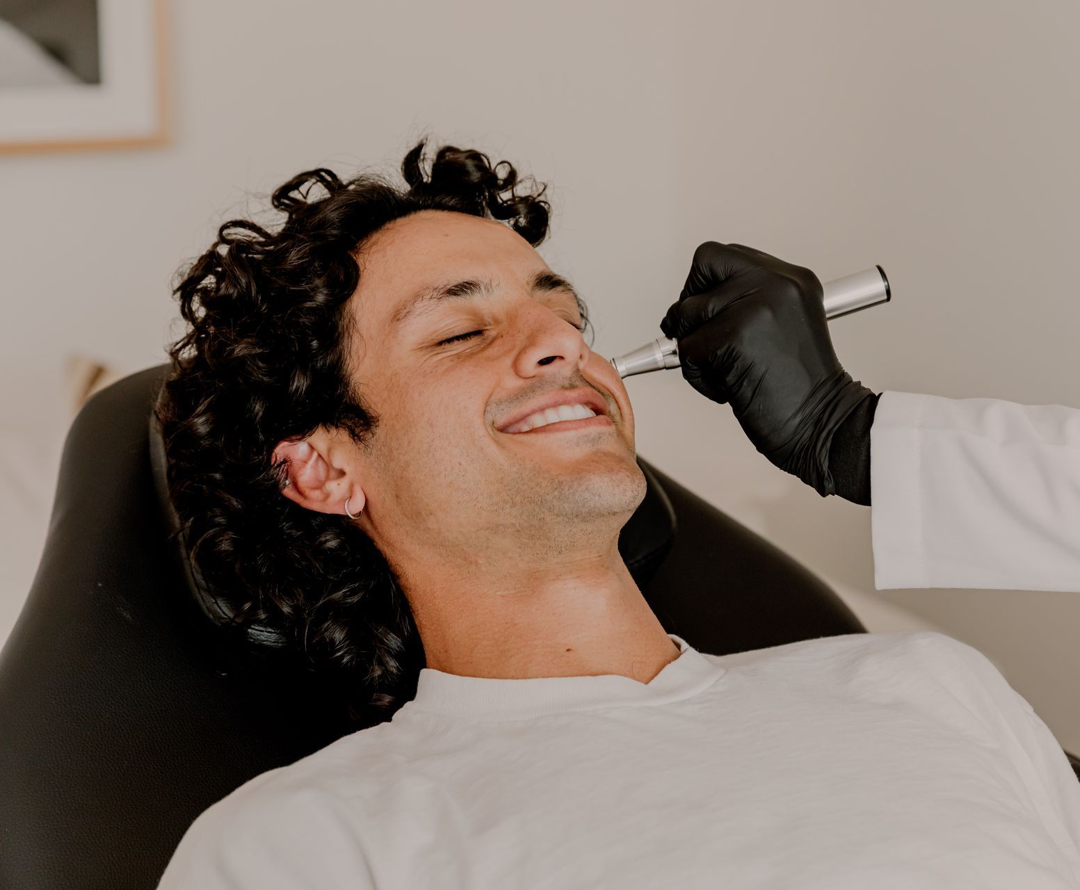 A doctor is giving a microneedling treatment to a man laying in a chair.