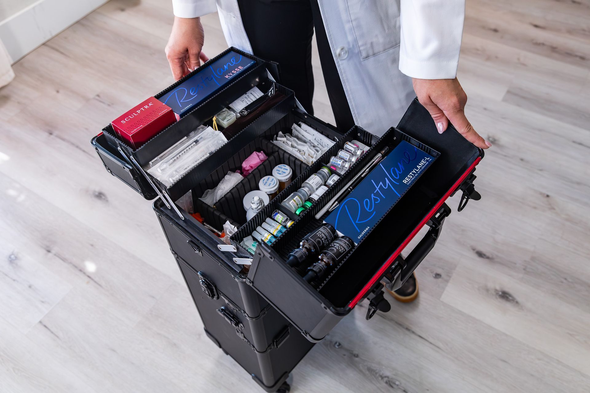 Person holding an open black rolling case filled with medical spa supplies, including vials and syringes.