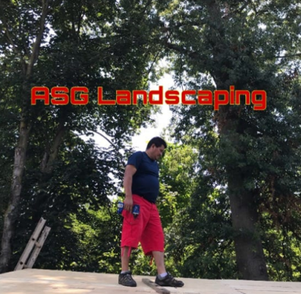 Man in red shorts near RSG Landscaping logo, outdoors, looking down.