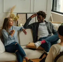 A therapist sitting in a chair facing two people seated on a couch, all engaged in an active conversation.