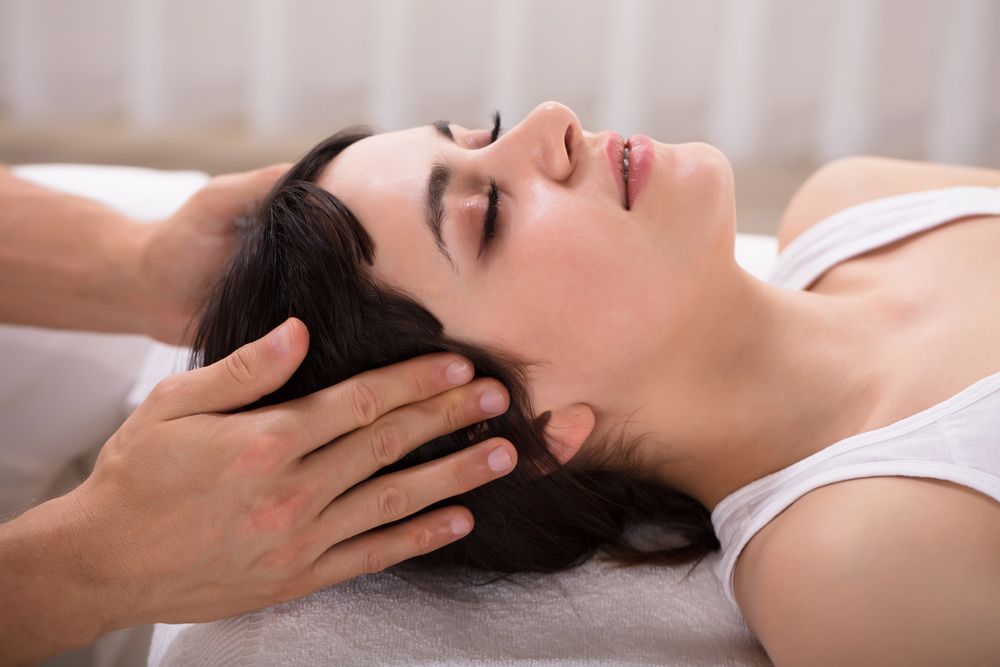 Una persona recibe un masaje en la cabeza mientras está tumbada sobre una toalla, con los ojos cerrados, en un entorno de spa.