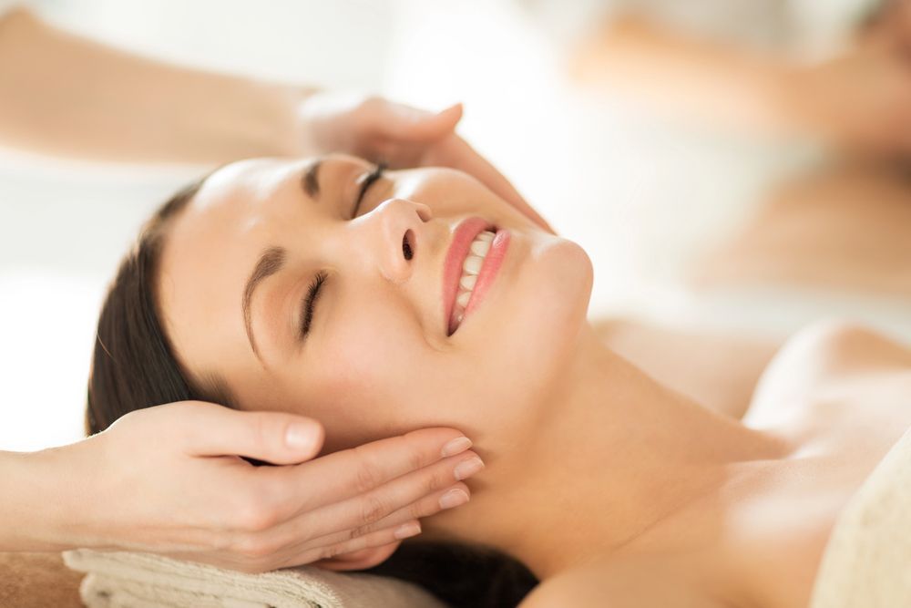 Mujer relajándose durante un masaje facial, con los ojos cerrados y una suave sonrisa.