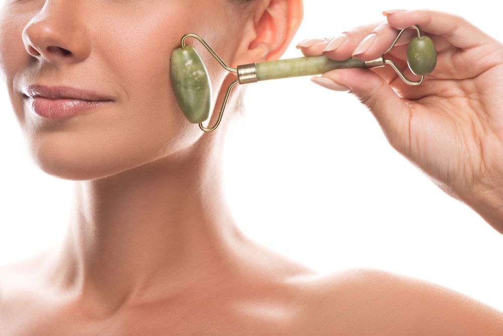 Mujer usando un rodillo facial de jade verde en su mejilla y mandíbula.