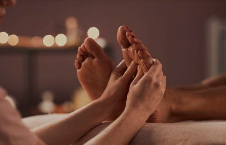 Primer plano de varios pies siendo sostenidos y masajeados en una camilla de spa en una habitación con iluminación tenue.