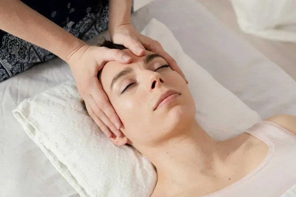 Mujer relajándose durante un masaje facial, con los ojos cerrados y una suave sonrisa.