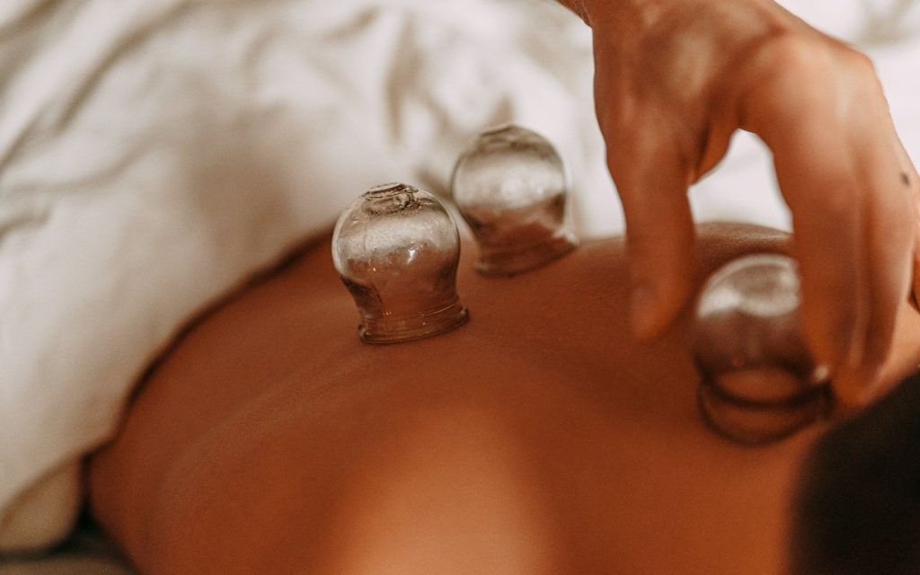 Unas manos masajean la espalda de una persona en una camilla de spa en una habitación cálida y con iluminación tenue.