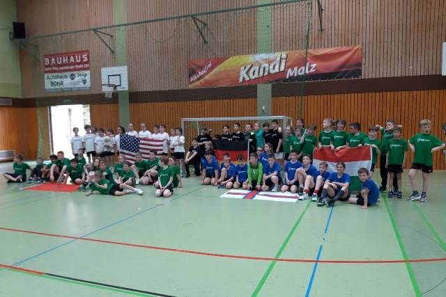 Eine Gruppe von Kindern posiert in einer Turnhalle für ein Foto unter einem Banner mit der Aufschrift „Kandi“