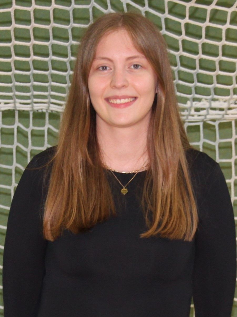 Eine junge Frau steht vor einem Tornetz und lächelt.