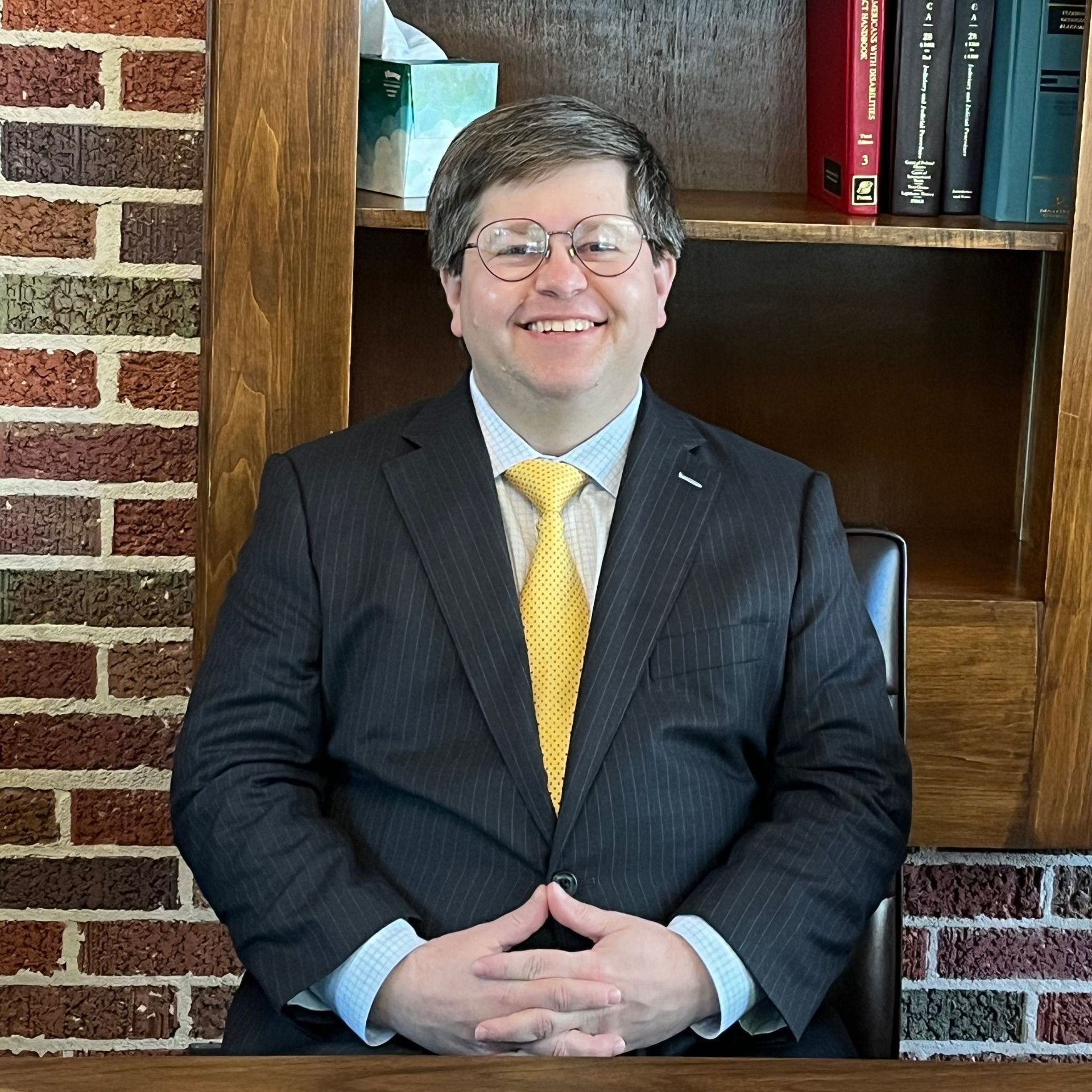 A man in a suit and tie is sitting at a desk in front of a brick wall.