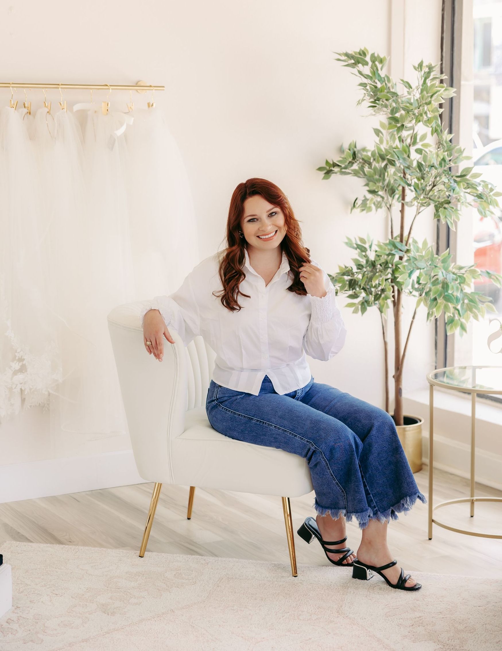 A woman in a white shirt and blue jeans is sitting in a chair.