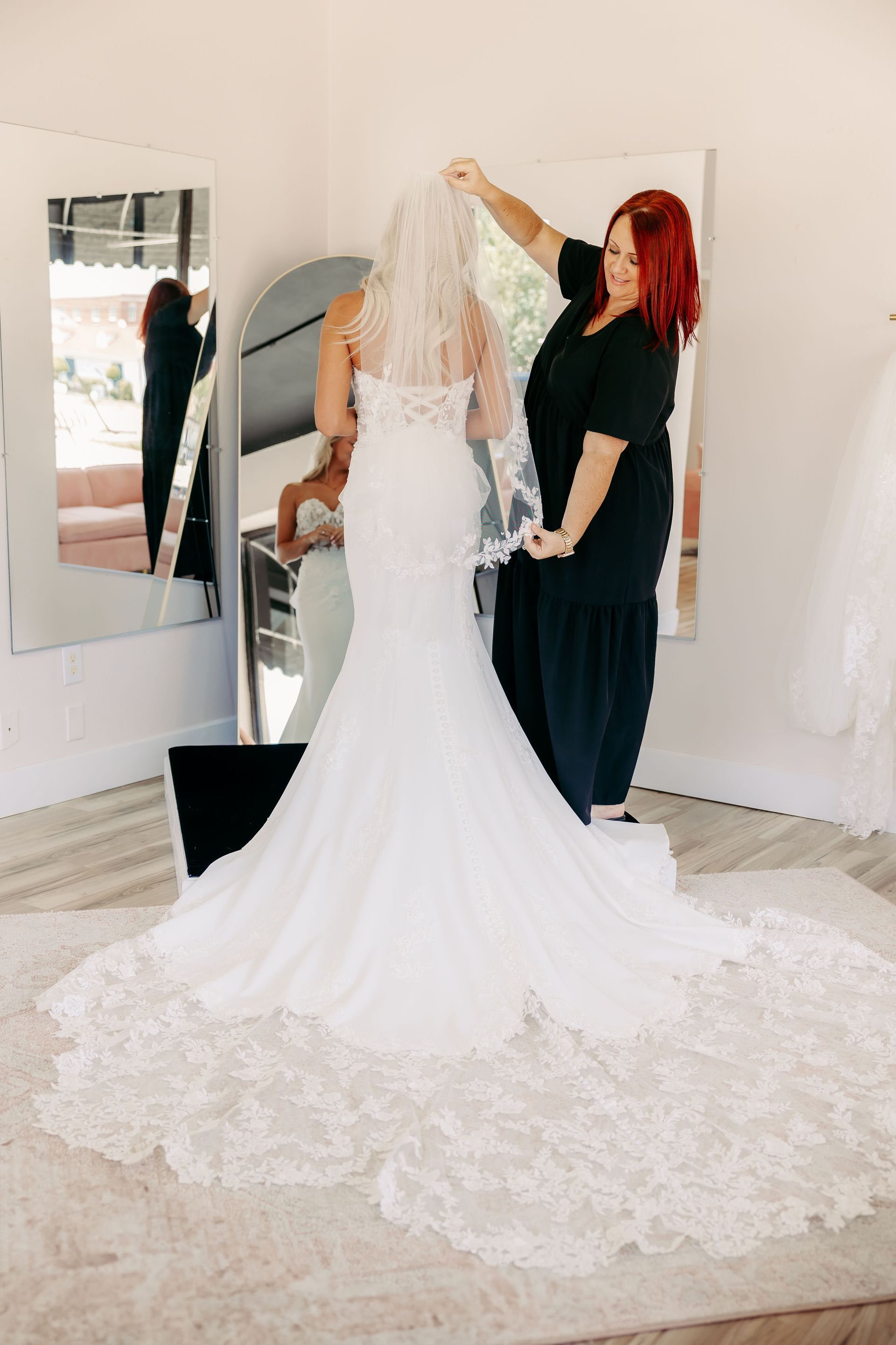 A woman is putting a veil on a bride 's head in front of a mirror.