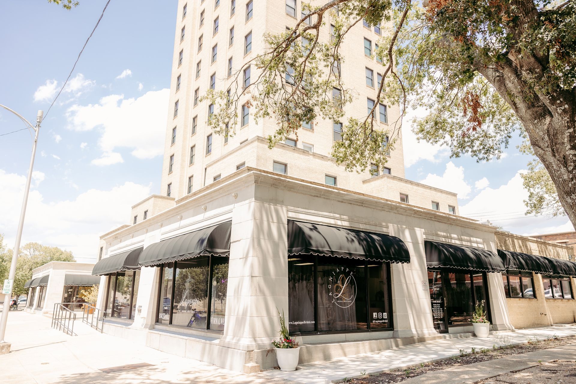 A large white building with black awnings and a tree in front of it.