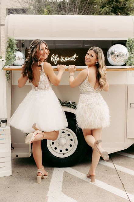 Two women in white dresses are standing next to each other in front of a trailer.