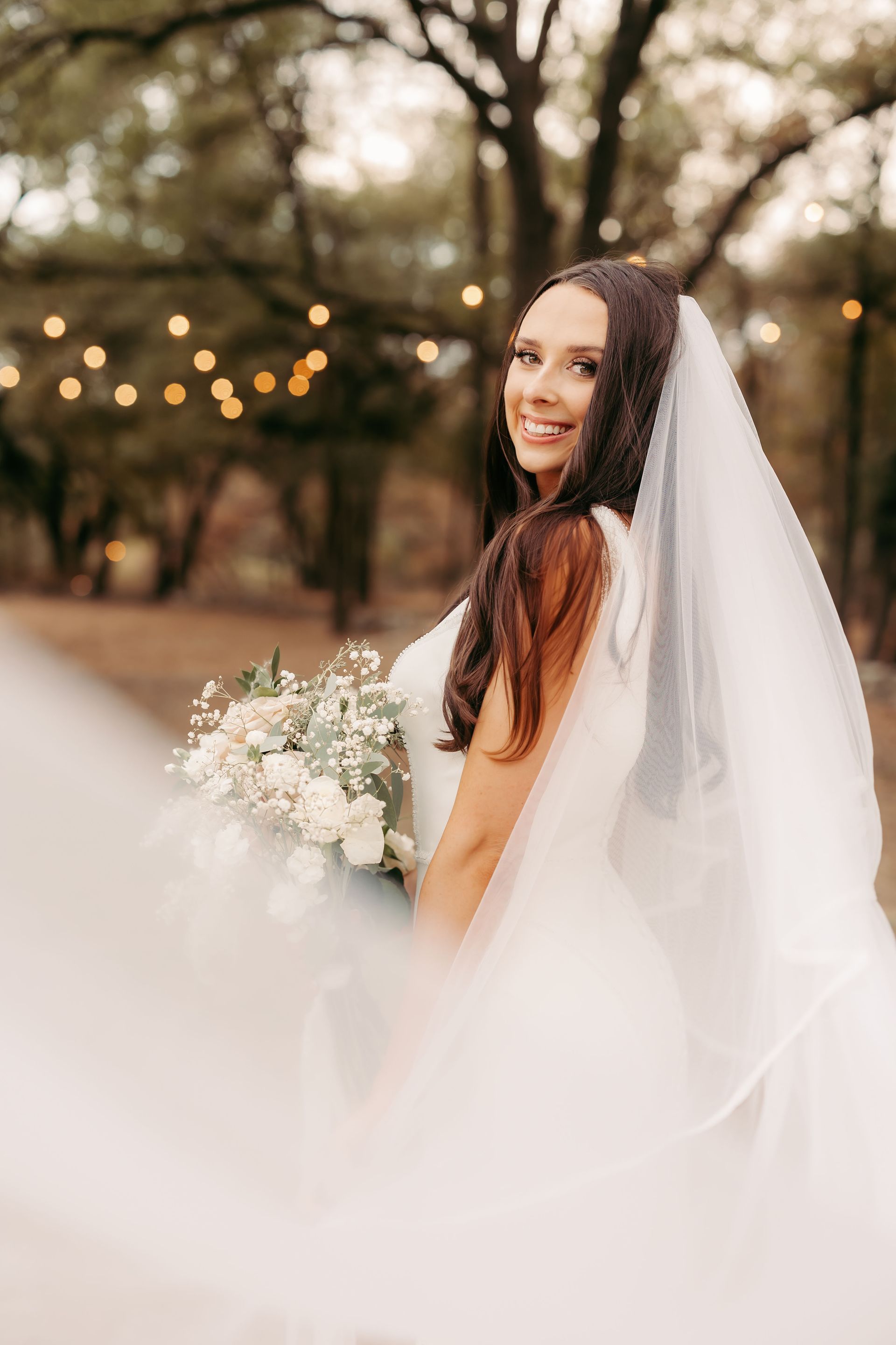 A bride and groom kissing while the bride holds a bouquet of white roses.