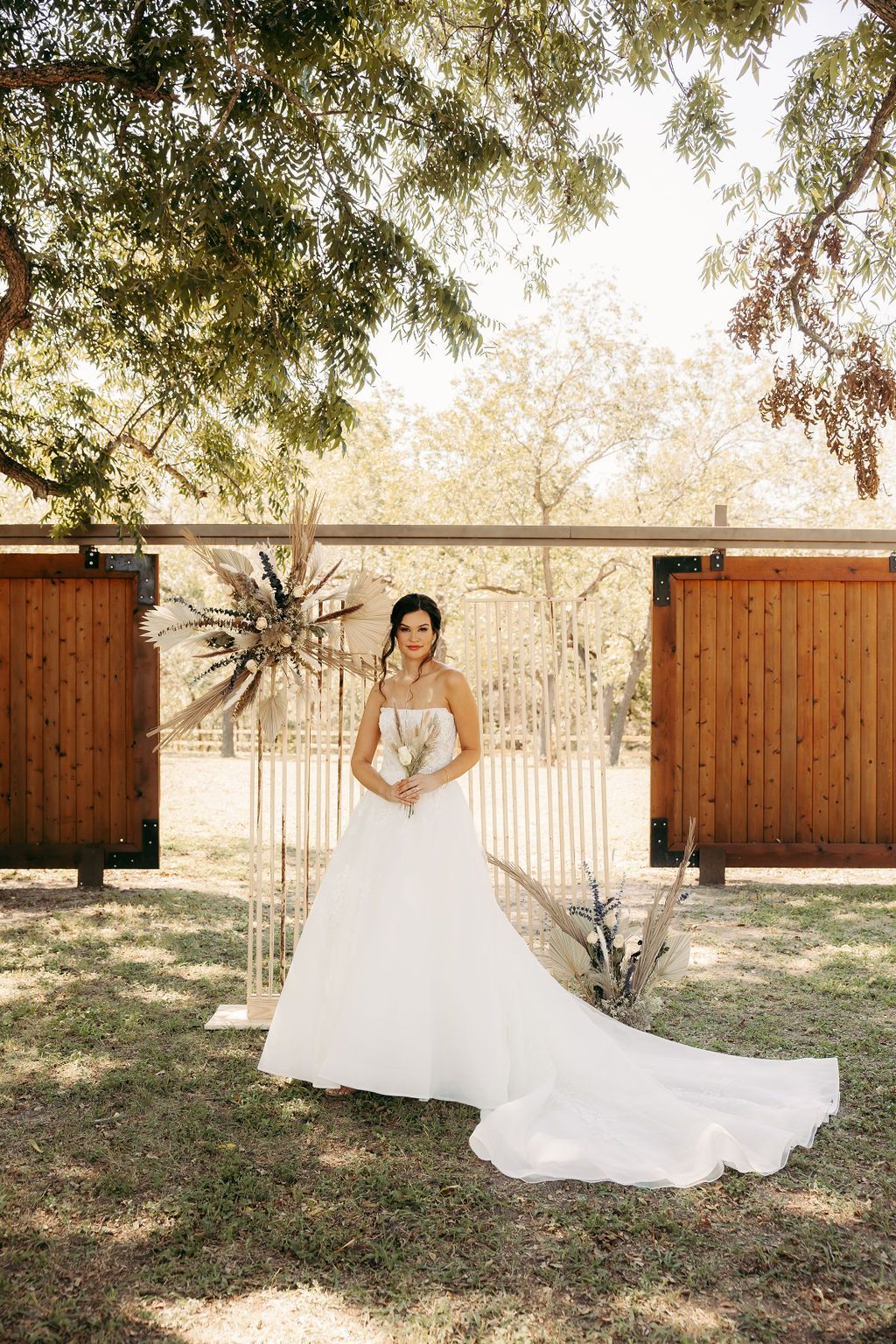 A bride in a wedding dress is standing in the grass in front of a wooden fence.