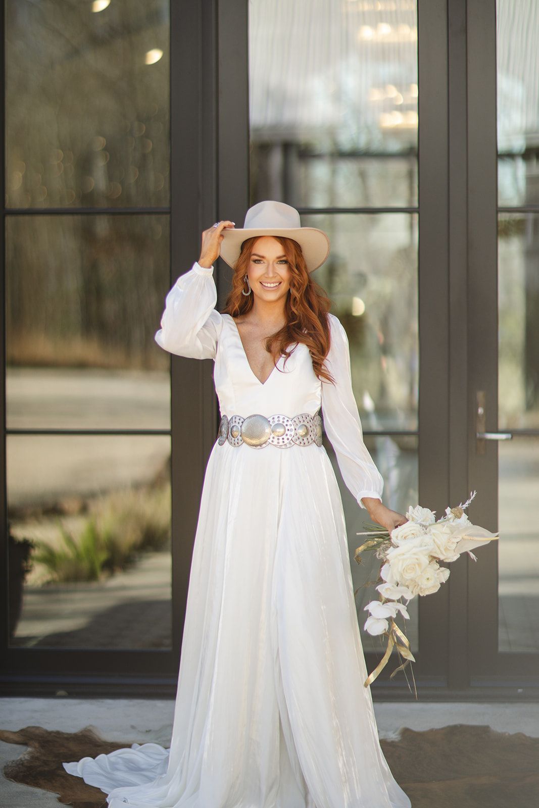 A woman in a white dress and cowboy hat is holding a bouquet of flowers.