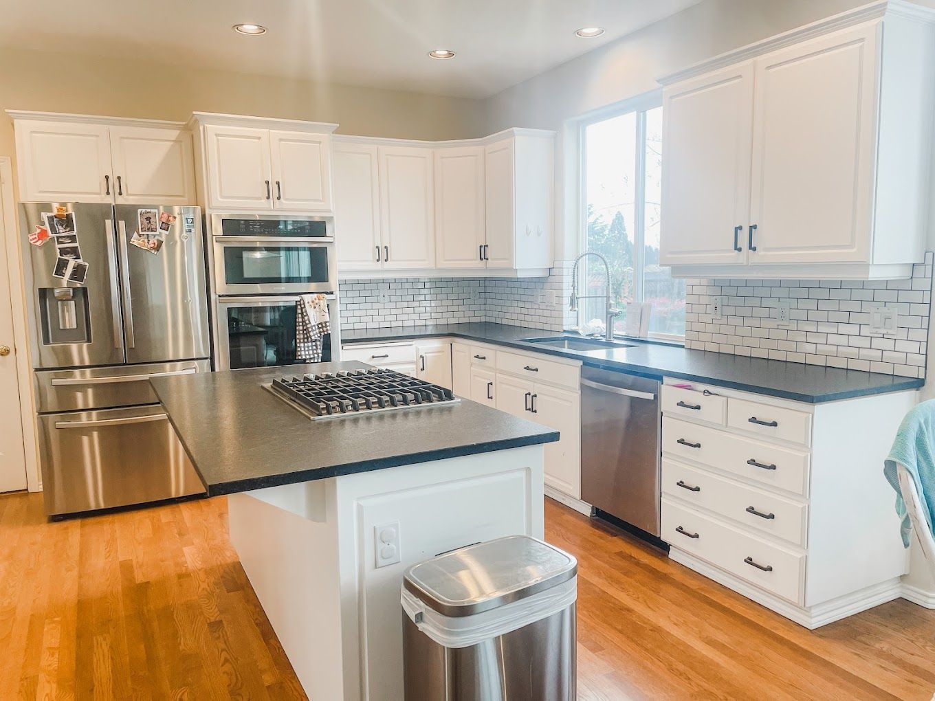A kitchen with white cabinets , stainless steel appliances , a large island and a trash can.