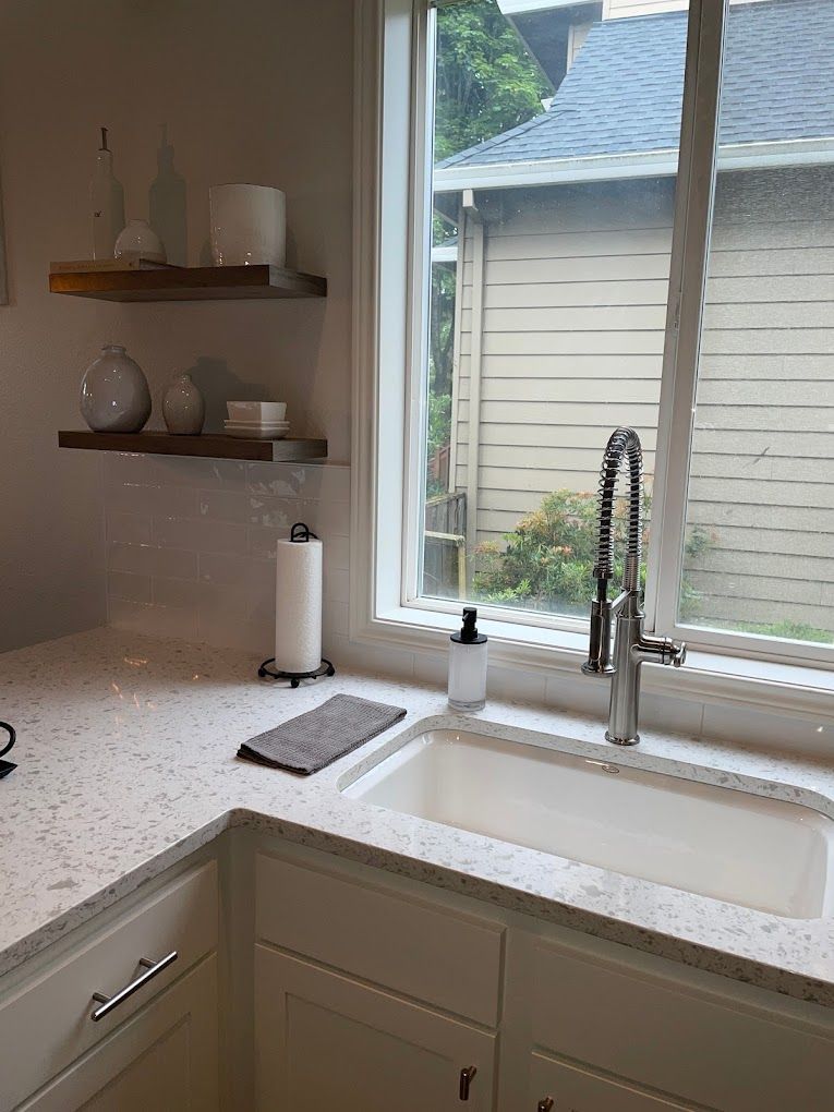 A kitchen with a sink and a window with a view of a house.
