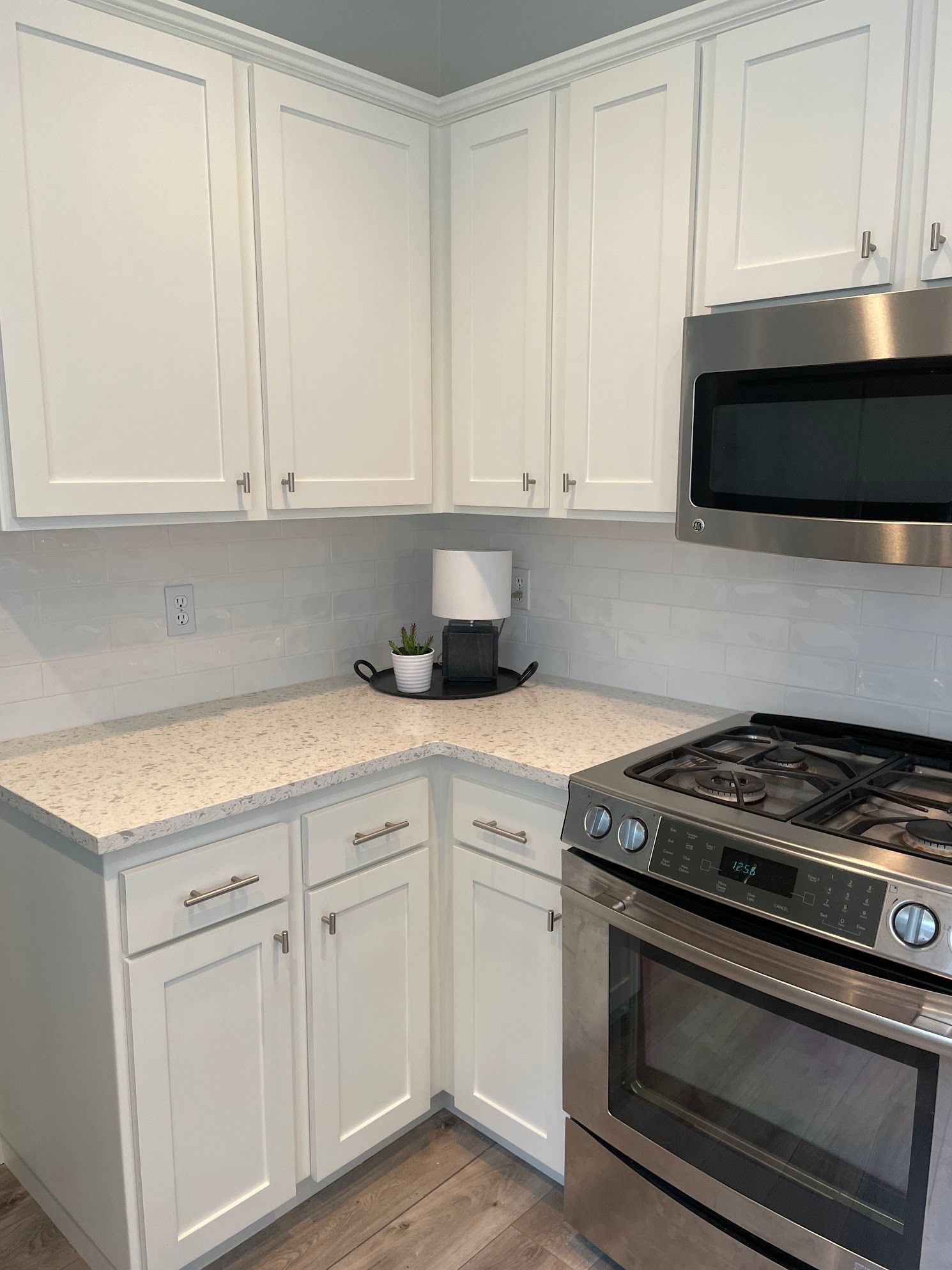 A kitchen with white cabinets , stainless steel appliances , a stove and a microwave.