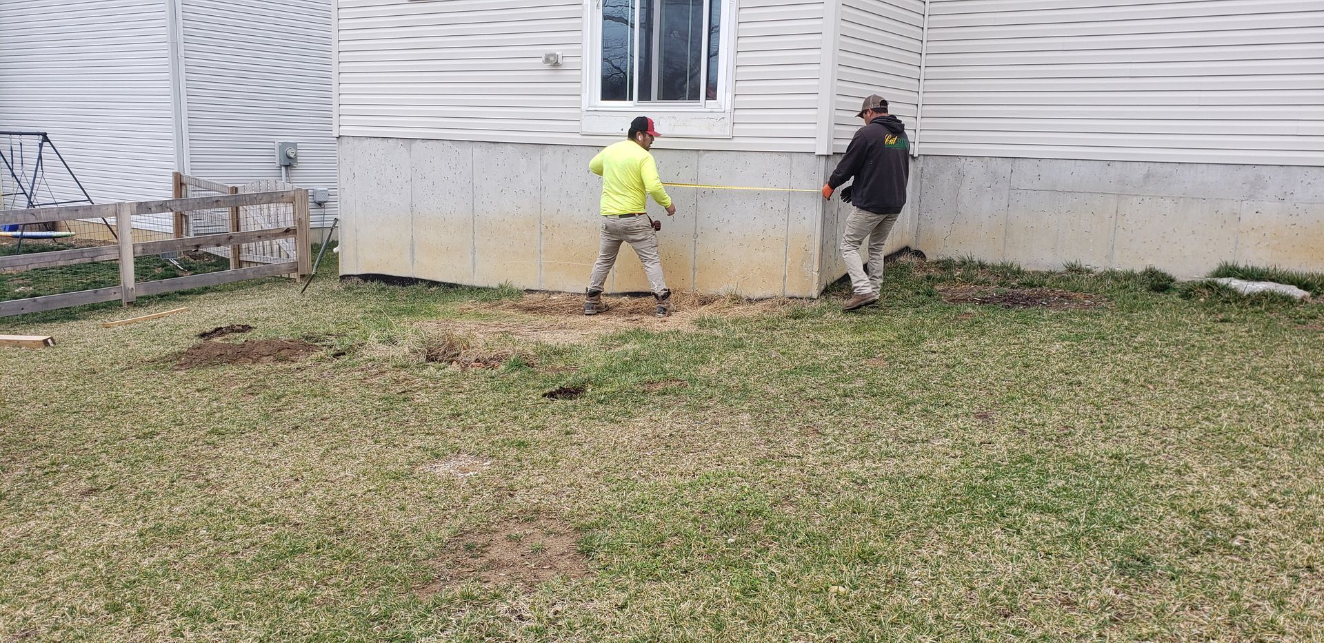 Two men are standing in front of a house in a yard.