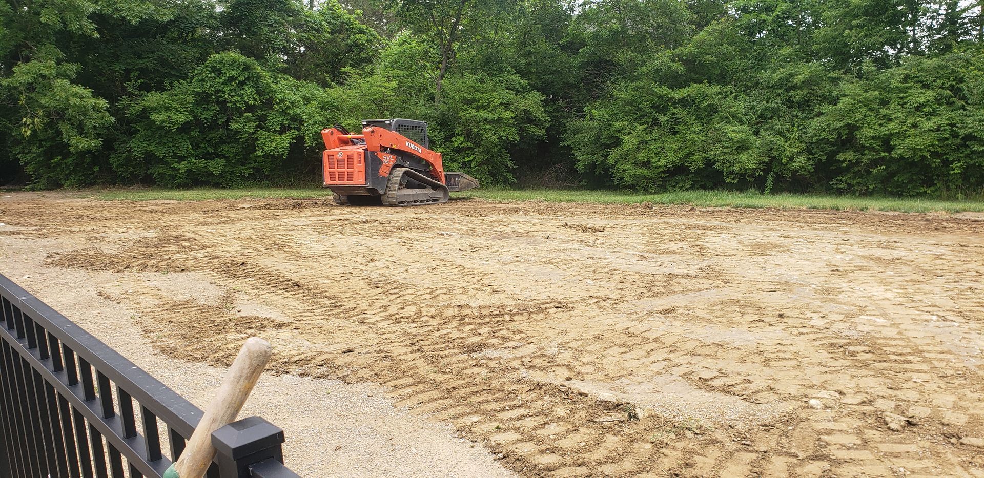 A bulldozer is moving dirt in a field next to a fence.