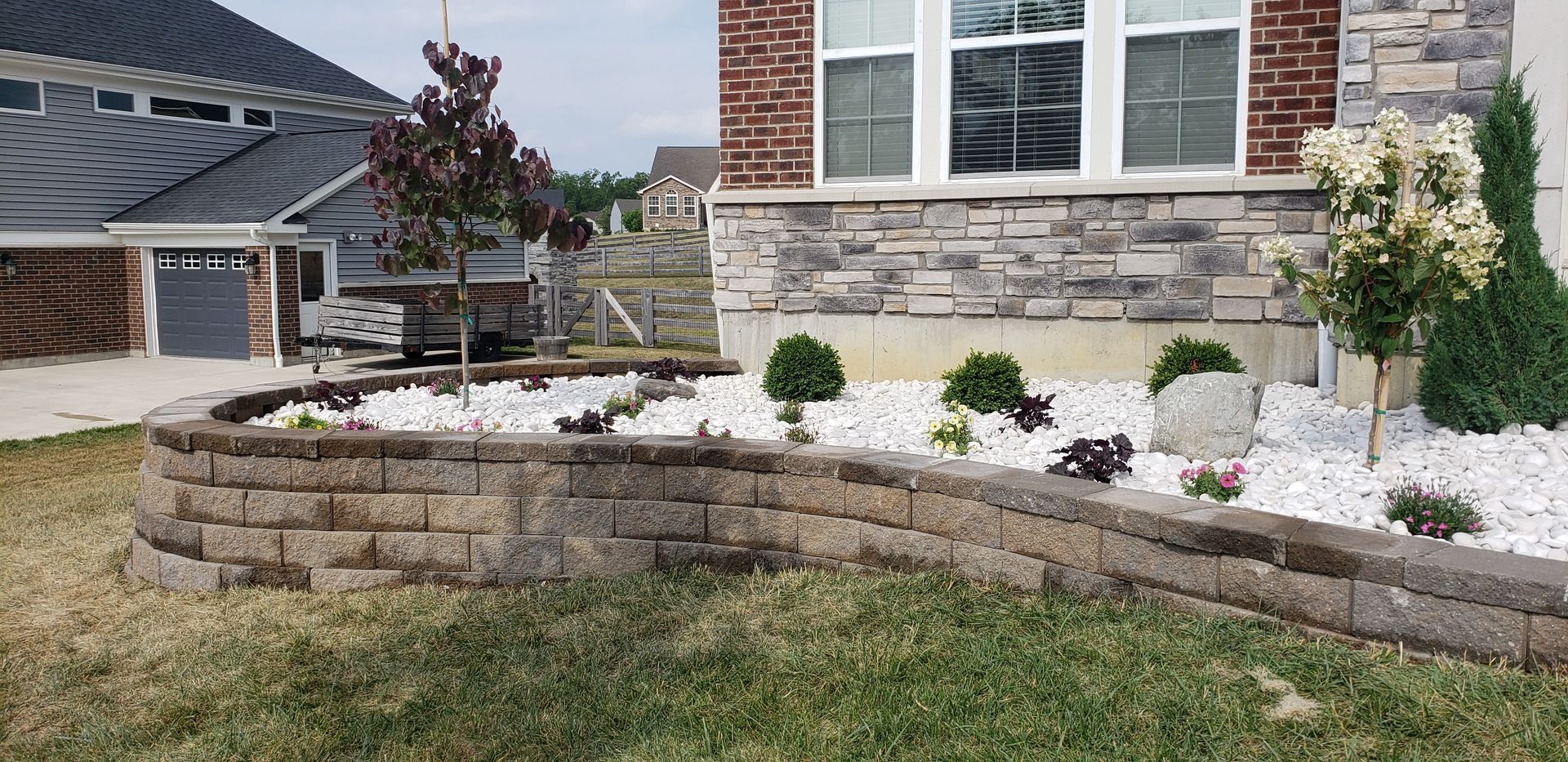 A brick wall in front of a house with a garden in front of it.