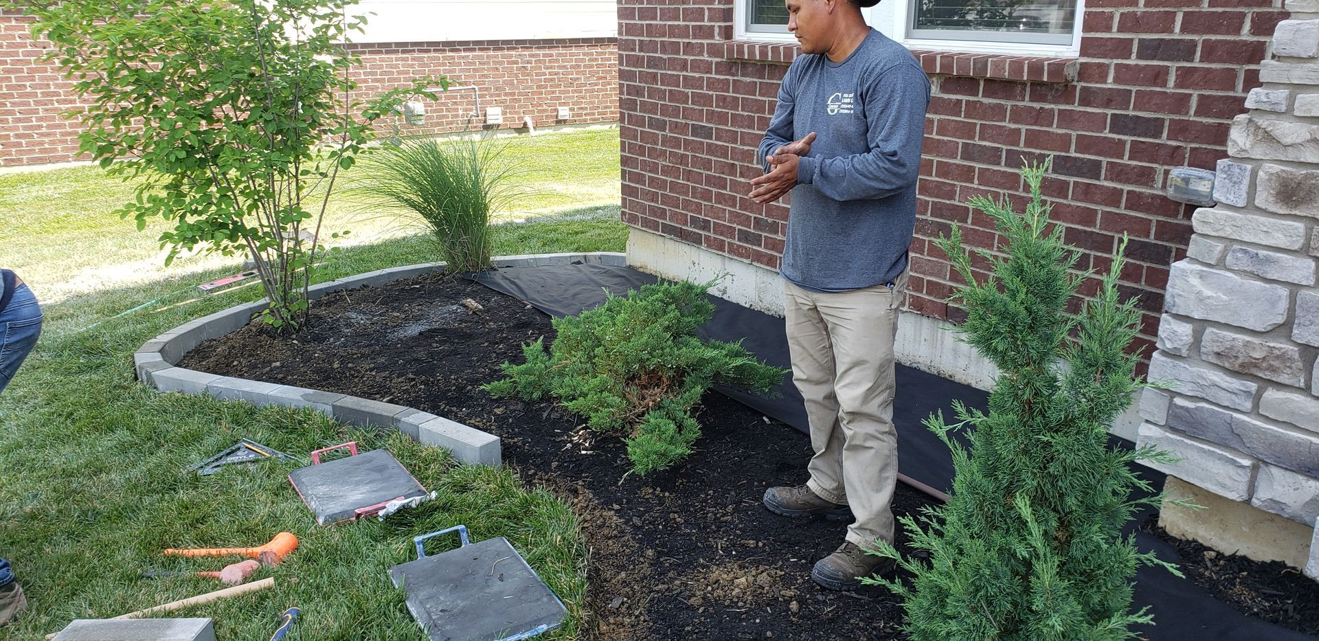 A man is standing in front of a brick house looking at a garden.